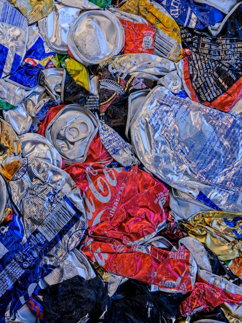 A black, metal public trash bin with a domed top is situated on a cobblestone street, surrounded by discarded litter including several empty beer bottles, crumpled paper, and food containers scattered