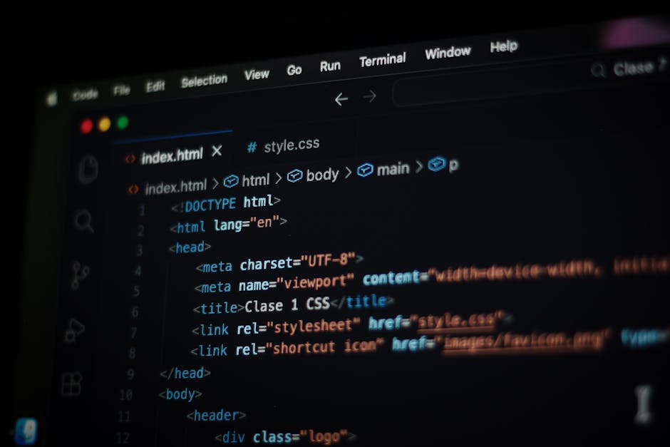 A person using a laptop with a silver body and a black keyboard, placed on a dark reflective surface. The laptop screen displays a coding interface with multiple lines of colorful code, including gree